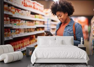 Smiling middle aged woman is shopping at a grocery store. An African American woman with a smart phone checks the list of necessary products in a grocery or supermarket with a sale and discounts on Wall mural