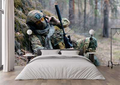 Special forces soldier during a clash in the forest. He calls his group's support on the walkie-talkie. Concept of modern military operations. Wall mural