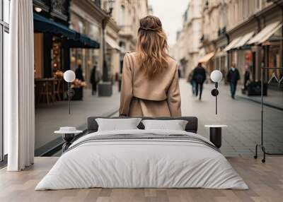 The concept of consumption and shopping. Photo of a stylish young blonde woman with shopping bags. She goes along a small European street with shops. View from the back. Wall mural