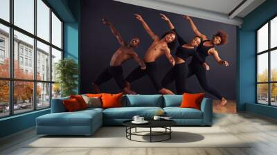 perfectly synchronised. a group of dancers performing a dramatic pose in front of a dark background. Wall mural