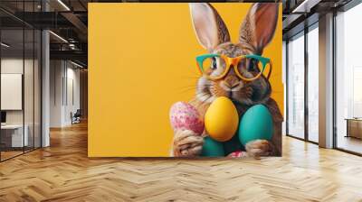 Easter bunny before a yellow solid colored background with easter eggs in his hand.  Wall mural