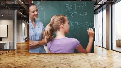 Improving on her mathematics. A pretty young teacher helping her student with a maths problem at the blackboard. Wall mural