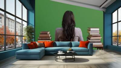 A person sitting at a desk, his back facing the viewer, surrounded by massive stacks of books, reflecting intense concentration and deep focus on study. Wall mural