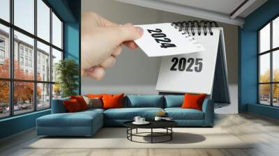 a woman's hand turns over a calendar sheet. year change from 2024 to 2025. Wall mural