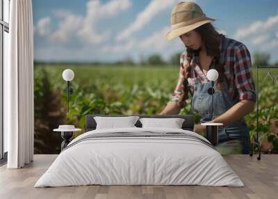 A woman in a straw hat is working in a field of green plants Wall mural