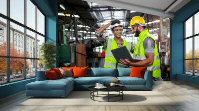 Industrial engineer wearing helmet and safe glasses, holding laptop computer for operating machinery at manufacturing plant factory, worker team working together in industry concept Wall mural