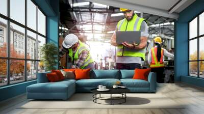 Industrial engineer wearing helmet and safe glasses, holding laptop computer for operating machinery at manufacturing plant factory, worker team working together in industry concept Wall mural