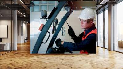 Industrial engineer worker wearing helmetand safe glasses, holding radio walkie talkie, driving forklift car at manufacturing plant factory industry concept Wall mural