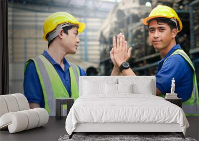 Portrait of two industrial engineer workers man wearing helmet doing high-five hand touch, standing at manufacturing plant factory with many engine parts as blurred background Wall mural