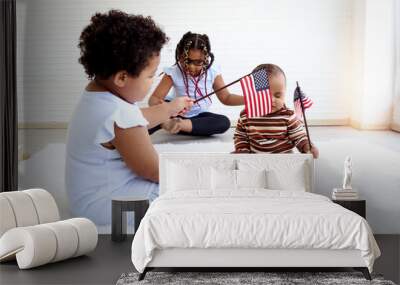 Two African American girl sister and infant baby sitting on floor in indoor living room, kid holding and waving American flag on 4th July to celebrate national Independence Day, Flag Day concept. Wall mural