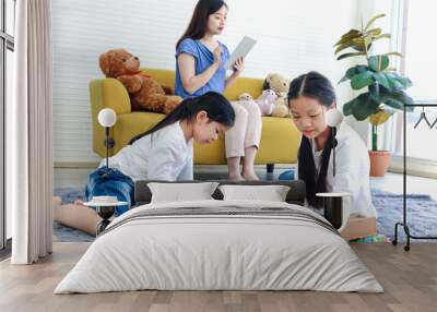 Two daughter girls playing with wooden block game (Jenga) together while mother sitting on sofa and surfing the internet, mom online working by using tablet, sister kid spending time together. Wall mural