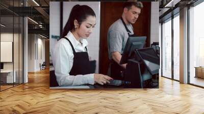 Young female and male  barista wearing apron standing behind coffee shop cashier counter, waitress and waiter staff working at cafe. Wall mural