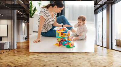 Laughing mother and little daughter playing colorful blocks, constructing tower, sitting on warm floor with underfloor heating, family enjoying leisure time Wall mural