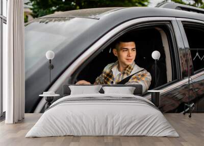 Young man driving a black car. Wall mural