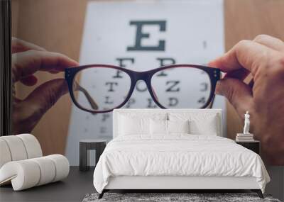 Hands holding sight glasses in front of optician sight chart. Eyesight optician concept Wall mural