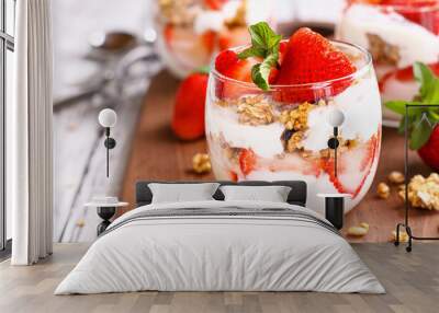 Healthy breakfast of strawberry parfaits made with fresh fruit, yogurt and granola over a rustic white table. Shallow depth of field with selective focus on glass jar in front. Blurred background. Wall mural