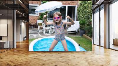 Female child in paddling pool in back garden making faces to the camera Wall mural