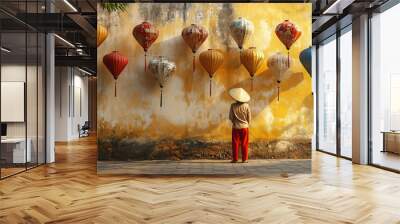 An Asian woman with a conical hat stands in front of a vibrant yellow wall adorned with colorful hanging lanterns, creating a beautiful and serene atmosphere. Wall mural