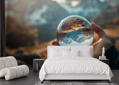 Hand holding a crystal ball with a reflection of a mountain landscape, symbolizing a unique and artistic perspective of nature Wall mural