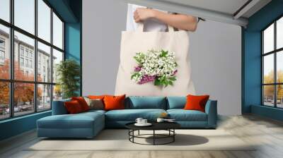 A woman holding a white canvas fabric tote bag with a print of a megaphone, for mockup blank template. on a colored background. Wall mural