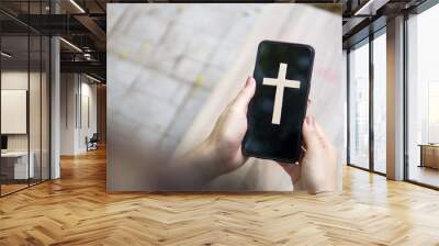 Woman's hand with cross in screen mobile phone. Concept of hope, faith, christianity, religion, church online. Wall mural