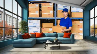 Portrait of woman delivery staff in blue uniform holding parcel box in warehouse Wall mural