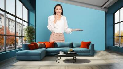 Young beautiful asian woman with smart casual cloth smiling and presenting copy space with surprise isolated on blue background Wall mural