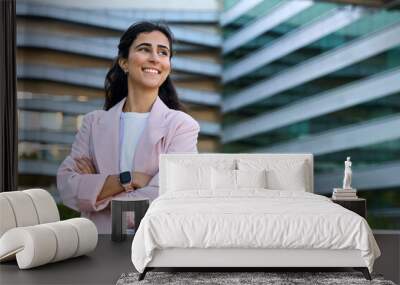 Confident portrait of young middle eastern Israel businesswoman standing with crossed hands at office building. Successful smiling indian or arabic woman in business suit looking aside. Copy space Wall mural