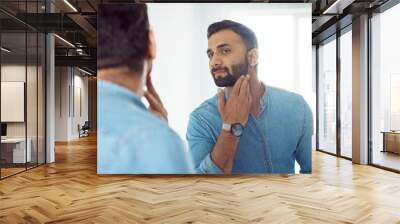 Curious thoughtful indian man touching beard on face looking at mirror Wall mural