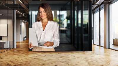 European businesswoman CEO holding laptop using fintech application standing at workplace in office. Smiling Latin Hispanic mature adult professional business woman using pc digital computer. Banner Wall mural