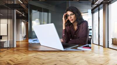 Focused young businesswoman looking at laptop pc computer screen having headache, migraine. Latin business woman holding hand near temples, feeling stressed and tired sitting at workplace in office Wall mural