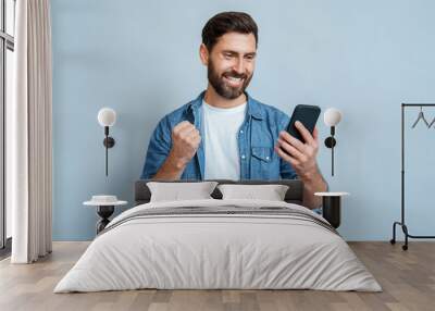 Happy delighted satisfied adult man looking at mobile phone screen gesturing yes winning pose, isolated background. Overjoyed excited joyful guy make winner gesture read message about happy good news Wall mural