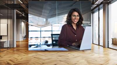 Happy latin hispanic young business woman working on laptop computer in company office. Smiling Indian entrepreneur manager businesswoman using pc for communication, learning at workplace. Copy space Wall mural