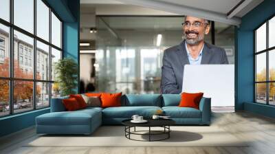 Portrait of mature Indian or Latin business man ceo trader using laptop computer, typing, working in modern office. Middle-age Hispanic smiling handsome businessman entrepreneur looking aside,dreaming Wall mural