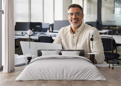 Portrait of mature Indian or Latin business man ceo trader using laptop computer, typing, working in modern office. Middle-age Hispanic smiling handsome businessman entrepreneur looking at camera. Wall mural