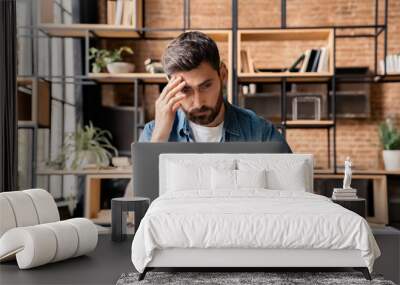 Serious frustrated businessman touching head with hand looking at laptop pc sitting at desk in home office. Puzzled freelance employee feeling tired exhausted, chronic work stress, having headache Wall mural