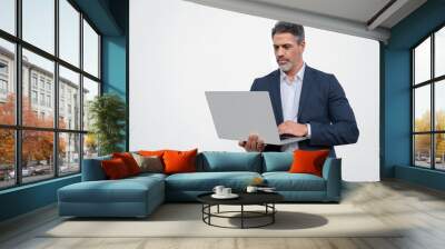 Serious handsome latin older man in formal suit holding desktop computer. Portrait of focused middle age mature businessman using pc laptop for business work. Isolated white background, copy space Wall mural