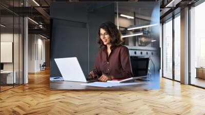 Smiling 30s latin hispanic middle-aged business woman working on laptop computer in modern office. Indian young businesswoman professional employee using pc doing online banking analysing at workplace Wall mural