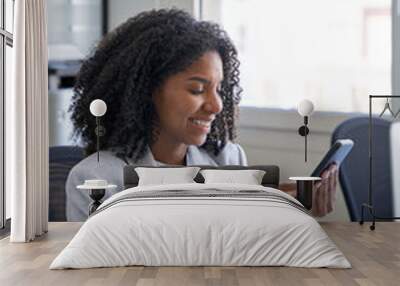 Vertical portrait of female entrepreneur businesswoman, successful African American business woman using smartphone, cellphone application, online communication, sitting at table in office indoors. Wall mural