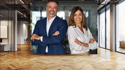 Vertical portrait of smiling mature Latin hispanic business man and European business woman standing arms crossed in office. Diverse colleagues, group team of confident professional business people. Wall mural