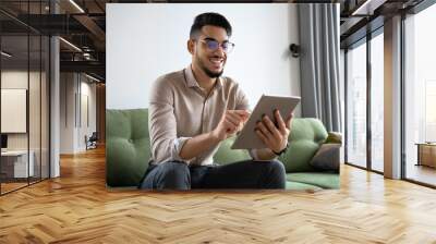 Young man using digital tablet computer sitting on sofa at home office Wall mural