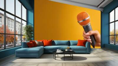 A hand holds a microphone against a bright yellow background. Wall mural