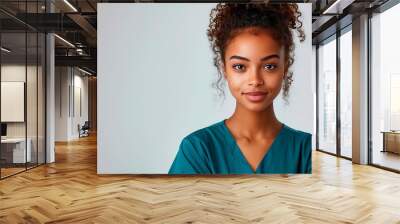 Smiling Young Woman With Curly Hair Wearing Teal Scrubs In Front of White Background Wall mural