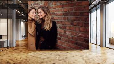 Two smiling women share a joyful moment by a brick wall in autumn, copy space for text Wall mural