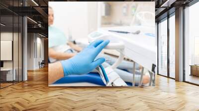 Close-up hand of dentist in the glove holds dental high speed turbine. The patient in blue chair at the background. Office where dentist conducts inspection and concludes. Wall mural