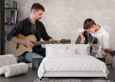 Two brothers learn to play acoustic guitar. The older brother tunes the guitar while the younger one runs his finger along the strings Wall mural