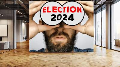 Close-up of a bearded man holding depicted binoculars to his eyes with the text ELECTION 2024 Wall mural