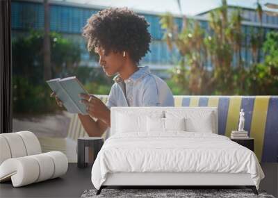 African girl reading book sitting on street bench close up. Student studying Wall mural