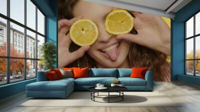 Playful girl having fun with lemon slices on yellow background. Cheerful woman Wall mural