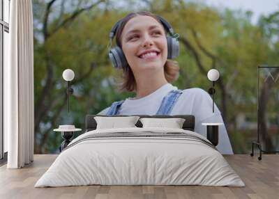 Smiling student listening headphones music holding phone on sunny street closeup Wall mural